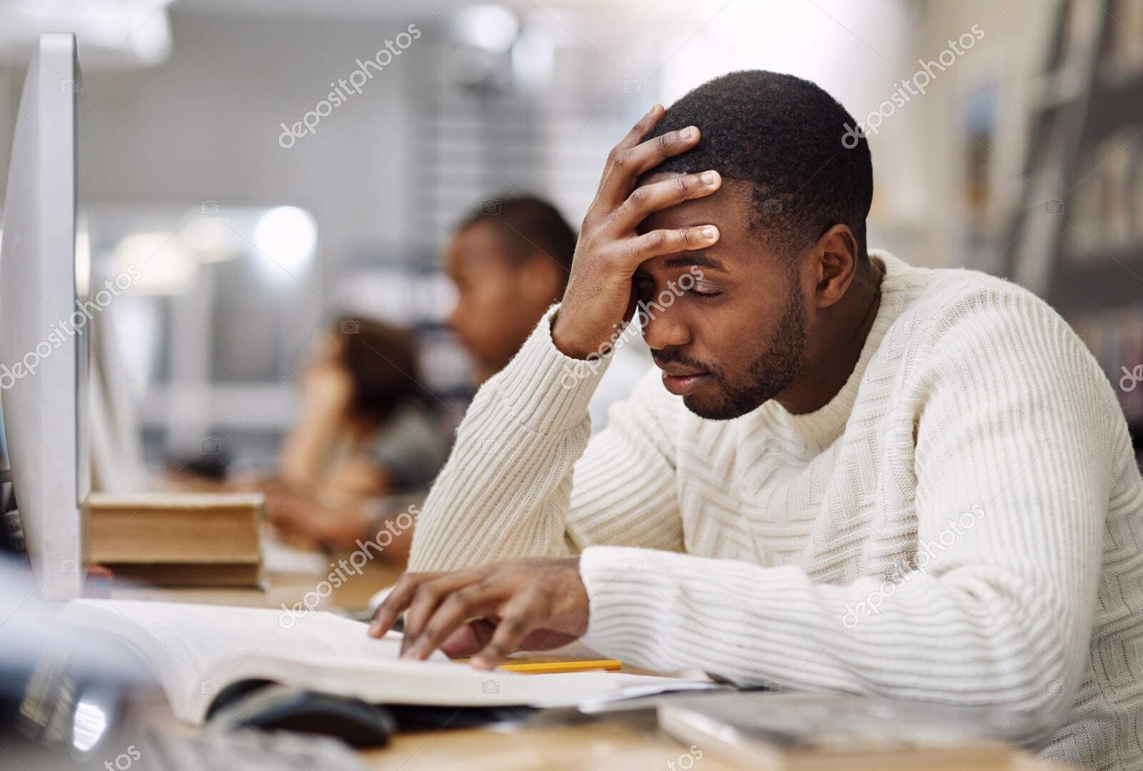 my head hurts from all this studying im doing. a young man studying in a college library and looking stressed.