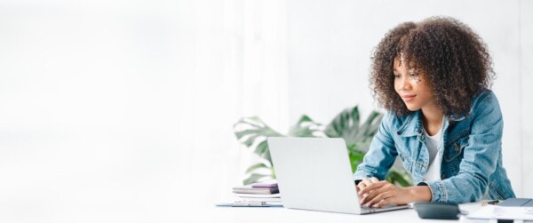 american teenage woman sitting in white office with laptop, she is a student studying online with laptop at home, university student studying online, online web education concept.