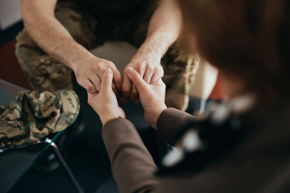 close up of psychotherapist holding hands with a soldier during counseling at her office.