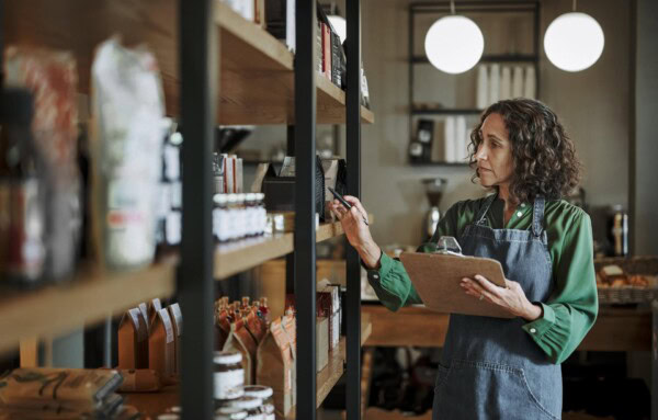 mature deli owner taking inventory on store shelves using a clipboard