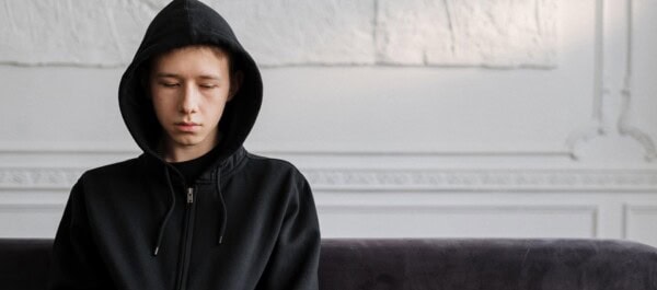 person wearing hooded jacket thinking deeply while sitting in a couch